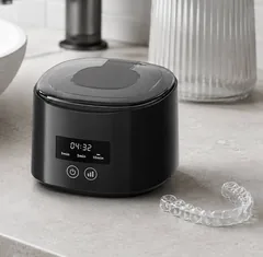 The DentaSonic ultrasonic cleaner on a pale marble bathroom counter, a clear retainer beside it