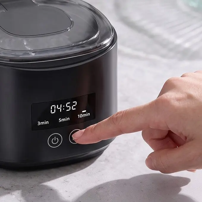 A finger pressing the cycle button on the DentaSonic cleaner, the display showing 3, 5 and 10 minutes